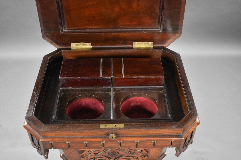 A William IV rosewood tea poy featuring a hinged lidded box top, carved openwork scrolls, a turned pedestal column, and a four-point base with scroll feet. View XI