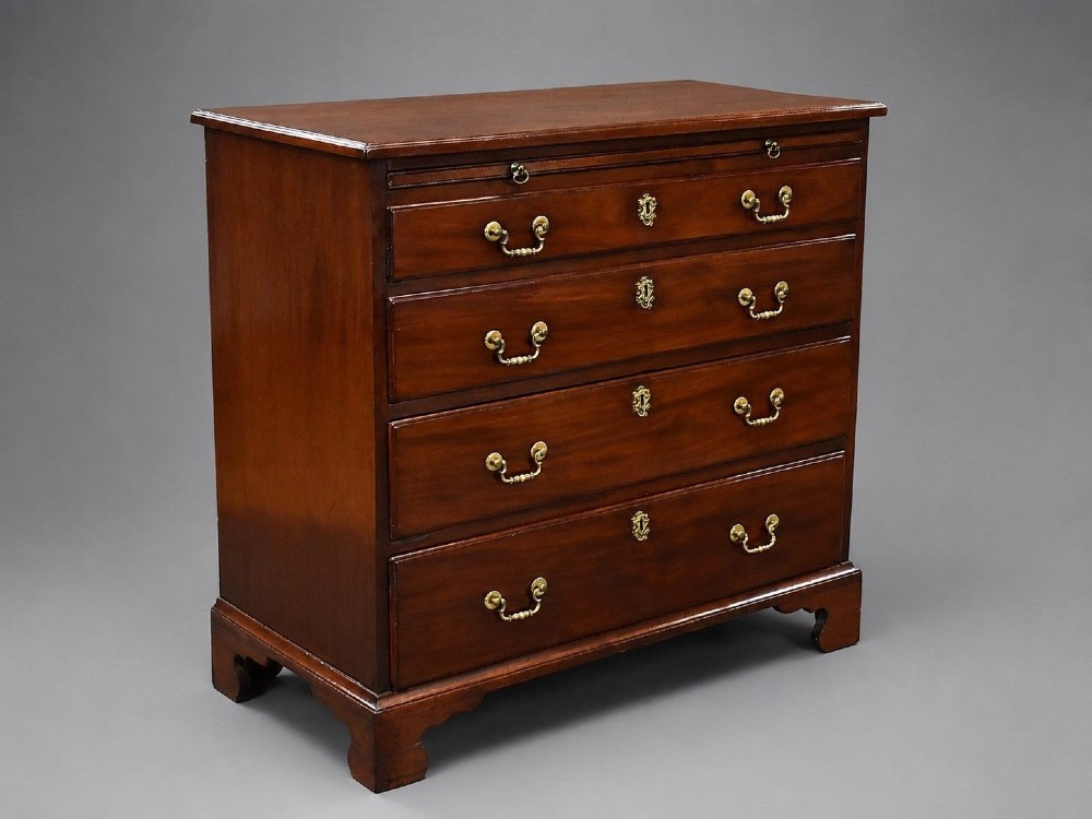 A George III mahogany bachelors chest of drawers featuring four graduated drawers, a pull-out brushing slide, brass swan-neck handles, and bracket feet.