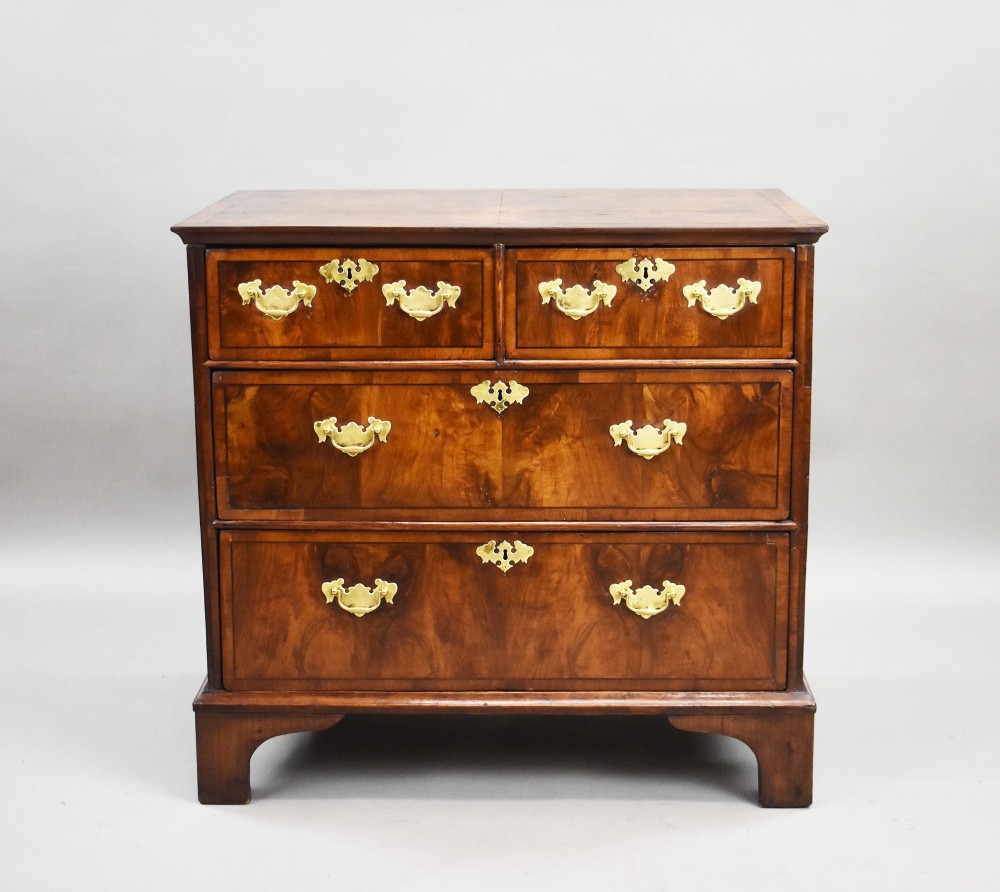 A Georgian burr walnut chest of drawers featuring two short over two long drawers with brass drop handles and pierced escutcheons, supported by bracket feet. View II