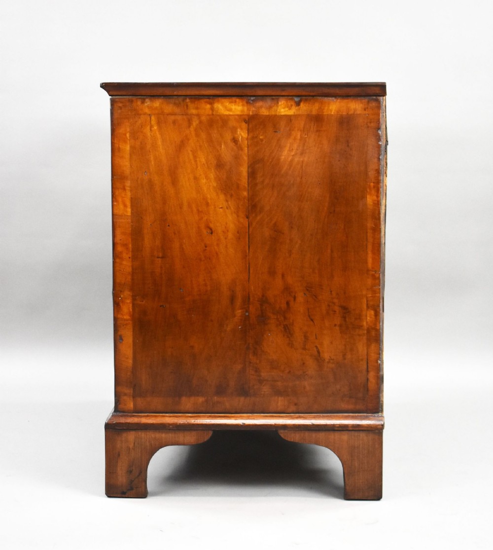 A Georgian burr walnut chest of drawers featuring two short over two long drawers with brass drop handles and pierced escutcheons, supported by bracket feet. View V