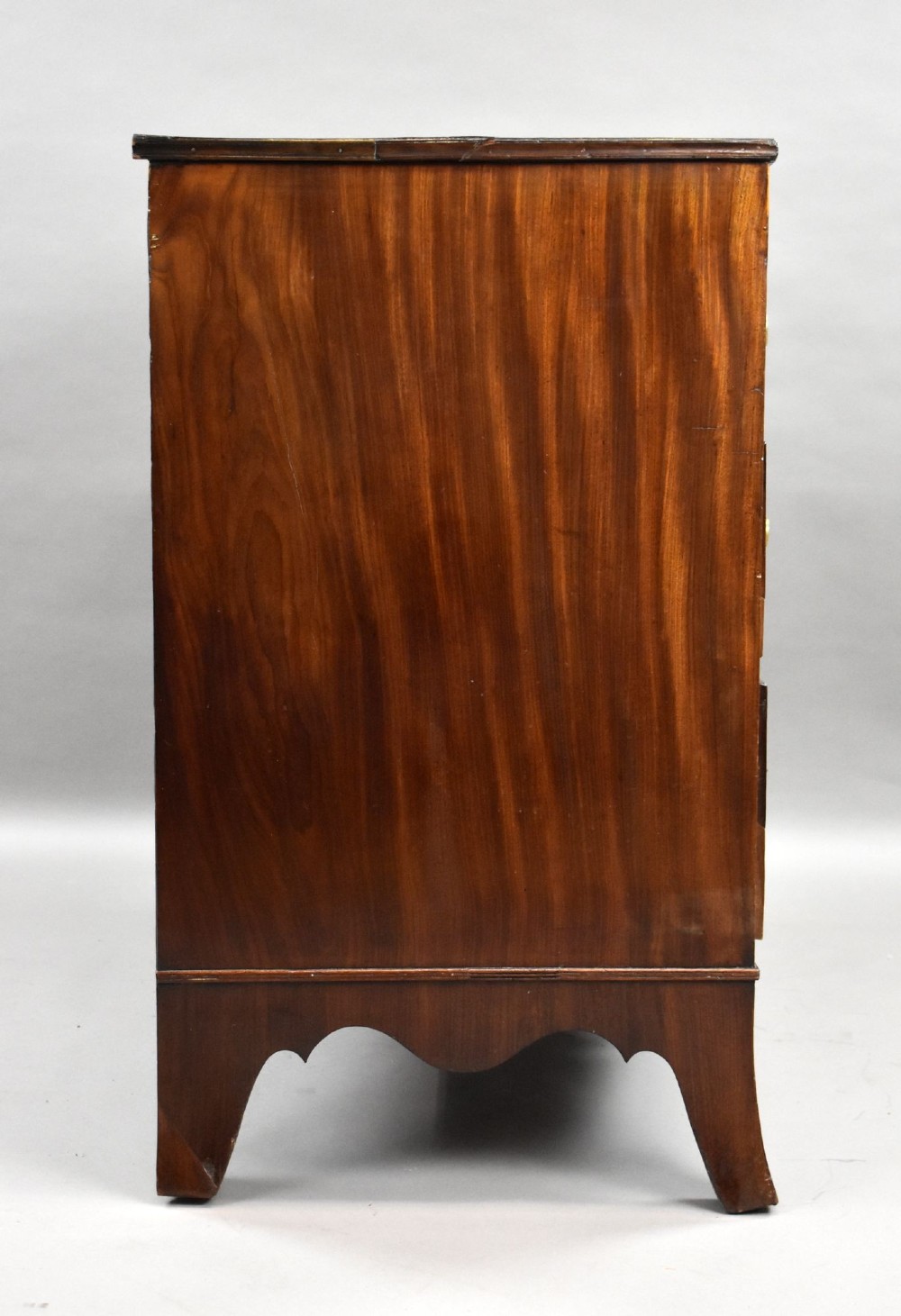 A Regency mahogany chest of drawers featuring three full-length drawers with brass knobs, bone keyhole escutcheons, flame veneer fronts, and a shaped apron base. View III