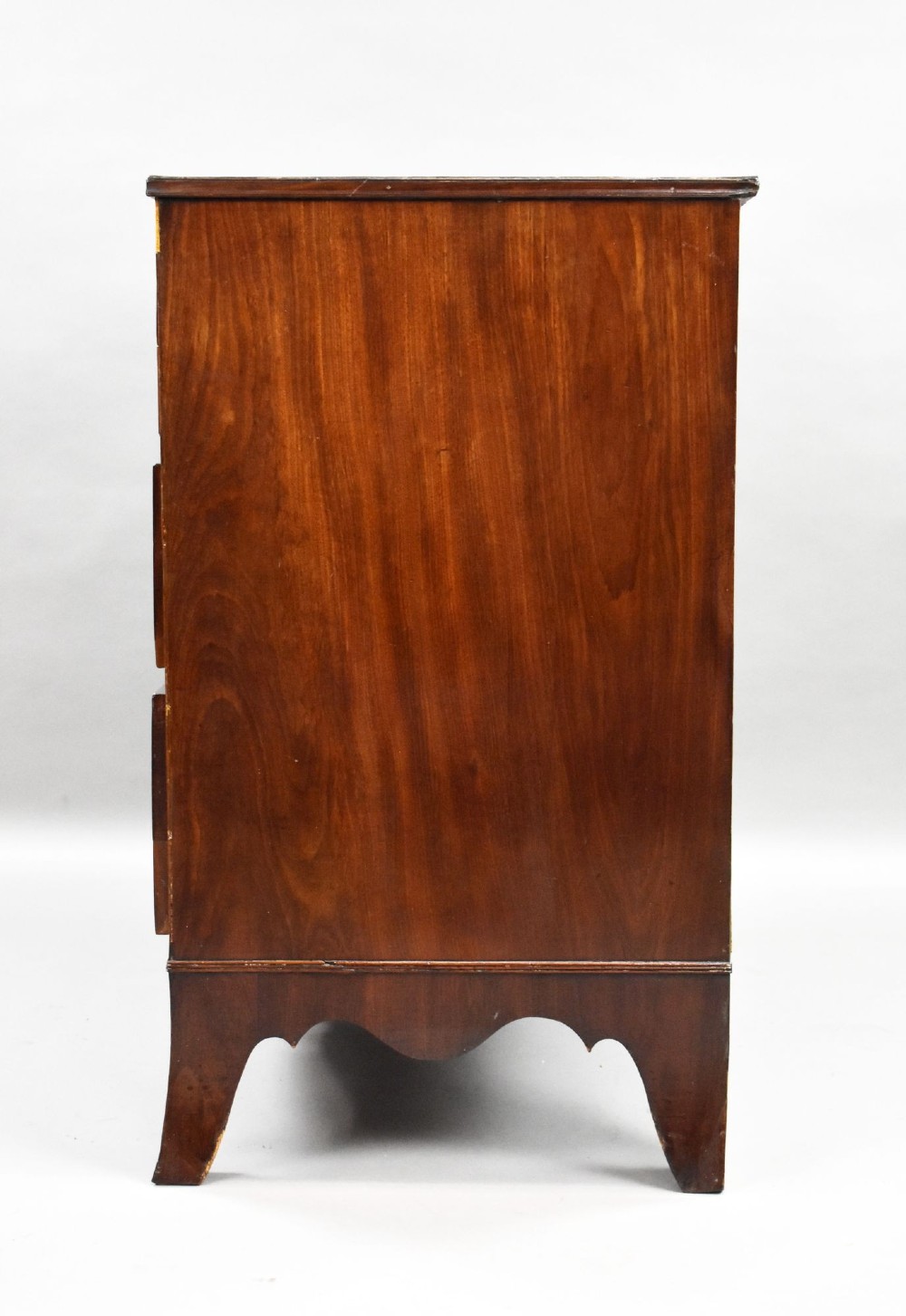 A Regency mahogany chest of drawers featuring three full-length drawers with brass knobs, bone keyhole escutcheons, flame veneer fronts, and a shaped apron base. View IV