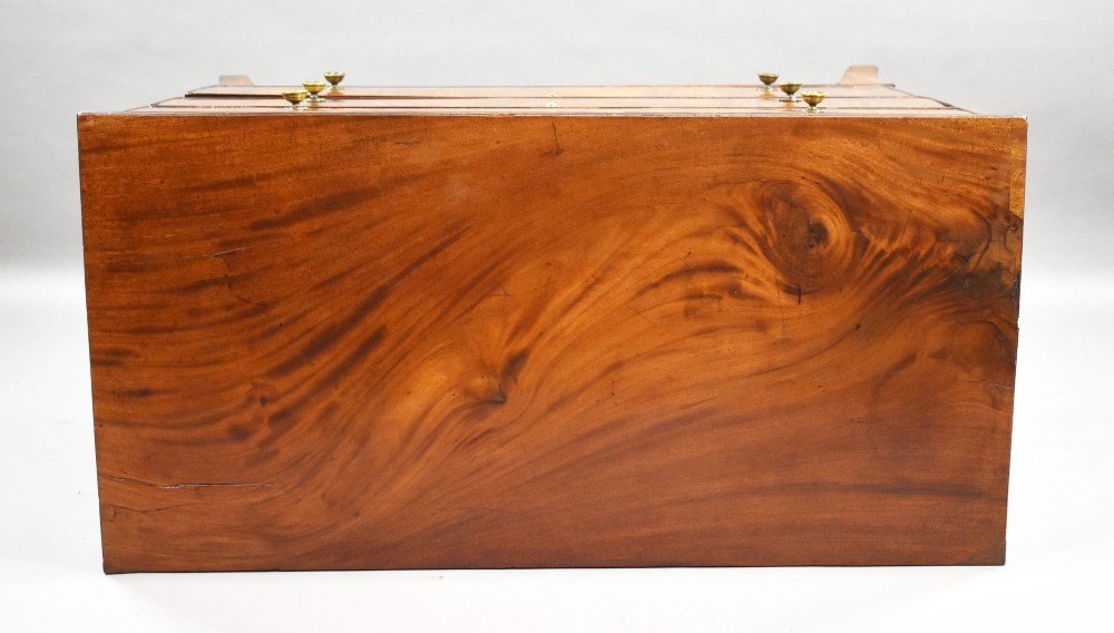 A Regency mahogany chest of drawers featuring three full-length drawers with brass knobs, bone keyhole escutcheons, flame veneer fronts, and a shaped apron base. View V
