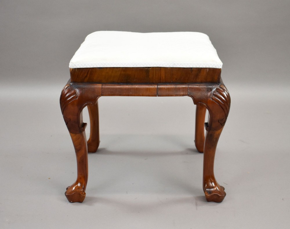 A square Queen Anne style walnut stool featuring cream textured fabric upholstery and carved cabriole legs with shell motifs. View II