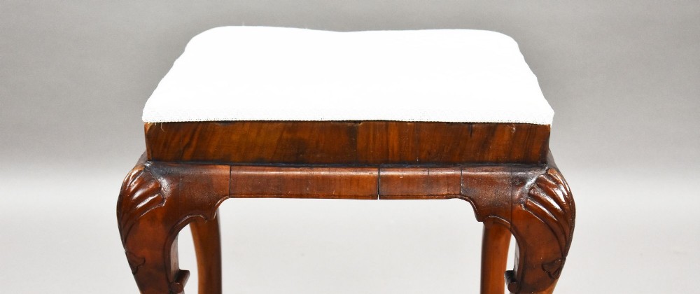A square Queen Anne style walnut stool featuring cream textured fabric upholstery and carved cabriole legs with shell motifs. View III