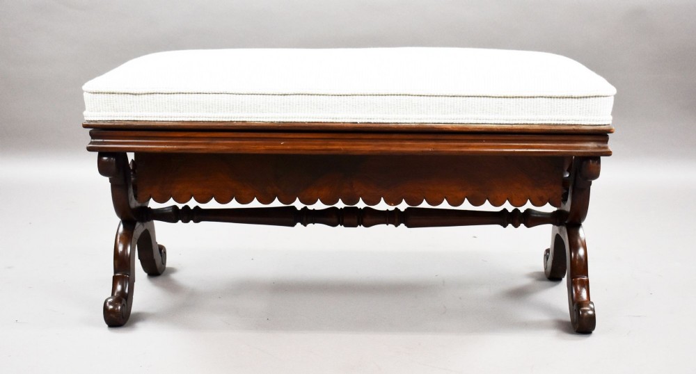 A William IV mahogany stool featuring a scalloped apron, carved scroll end supports, a turned central stretcher, and an off-white upholstered seat cushion. View II