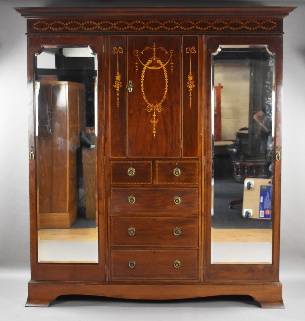 An Edwardian mahogany triple wardrobe featuring twin full-length mirror doors flanking a central inlaid cupboard and four drawers. View V