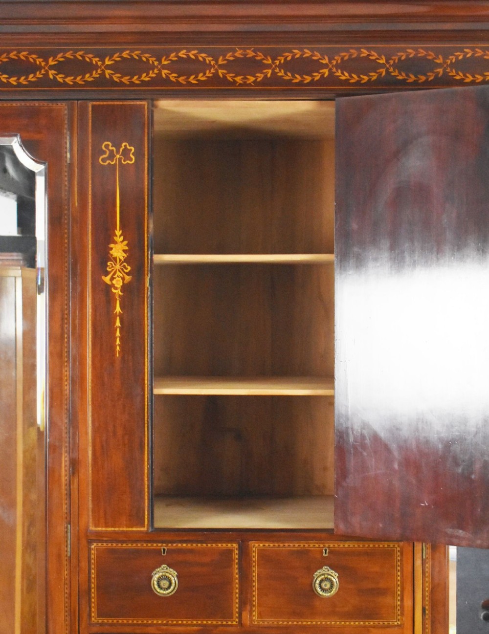 An Edwardian mahogany triple wardrobe featuring twin full-length mirror doors flanking a central inlaid cupboard and four drawers. View VII