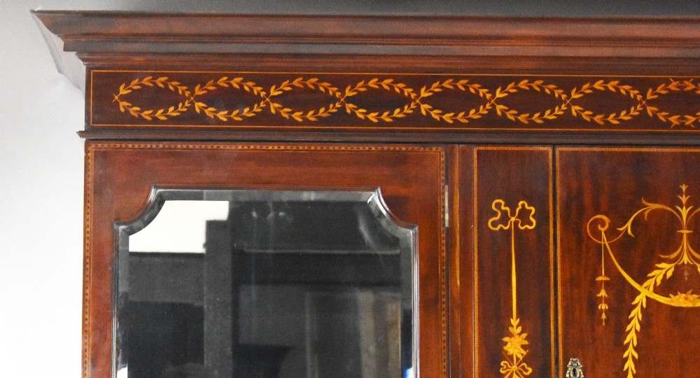 An Edwardian mahogany triple wardrobe featuring twin full-length mirror doors flanking a central inlaid cupboard and four drawers. View IX