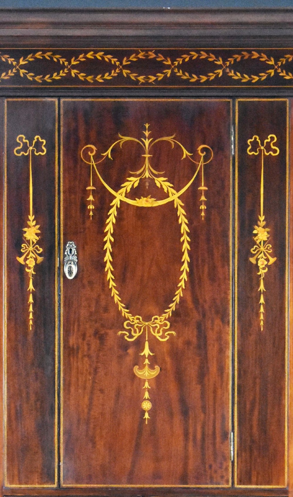 An Edwardian mahogany triple wardrobe featuring twin full-length mirror doors flanking a central inlaid cupboard and four drawers. View X