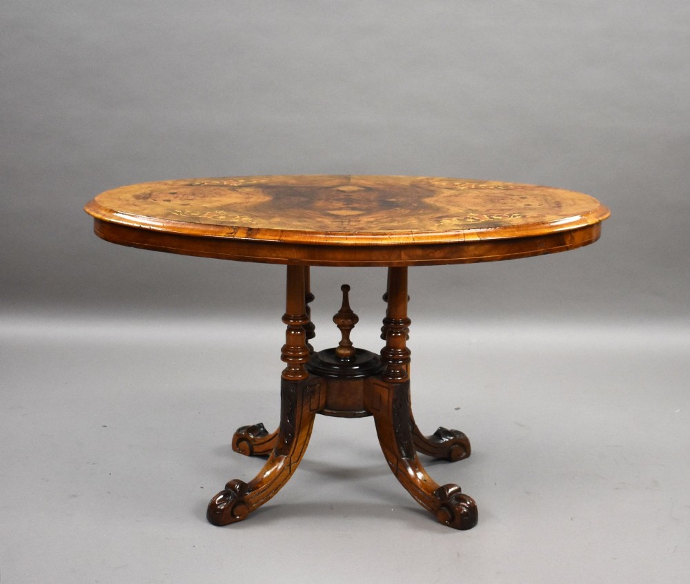 An oval Victorian burr walnut coffee table with floral marquetry inlay, four turned columns, and carved splayed feet. View II