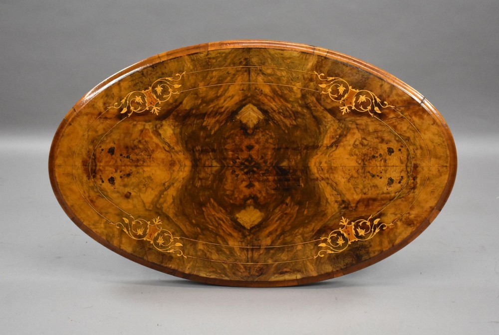 An oval Victorian burr walnut coffee table with floral marquetry inlay, four turned columns, and carved splayed feet. View IV