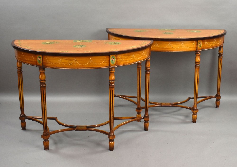 A pair of Sheraton Revival demi-lune console tables in golden satinwood with hand-painted floral garlands, fluted tapered legs, and decorative stretchers. View II