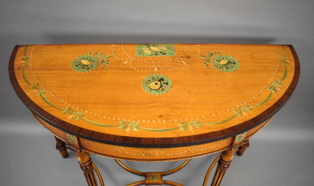A pair of Sheraton Revival demi-lune console tables in golden satinwood with hand-painted floral garlands, fluted tapered legs, and decorative stretchers. View VII