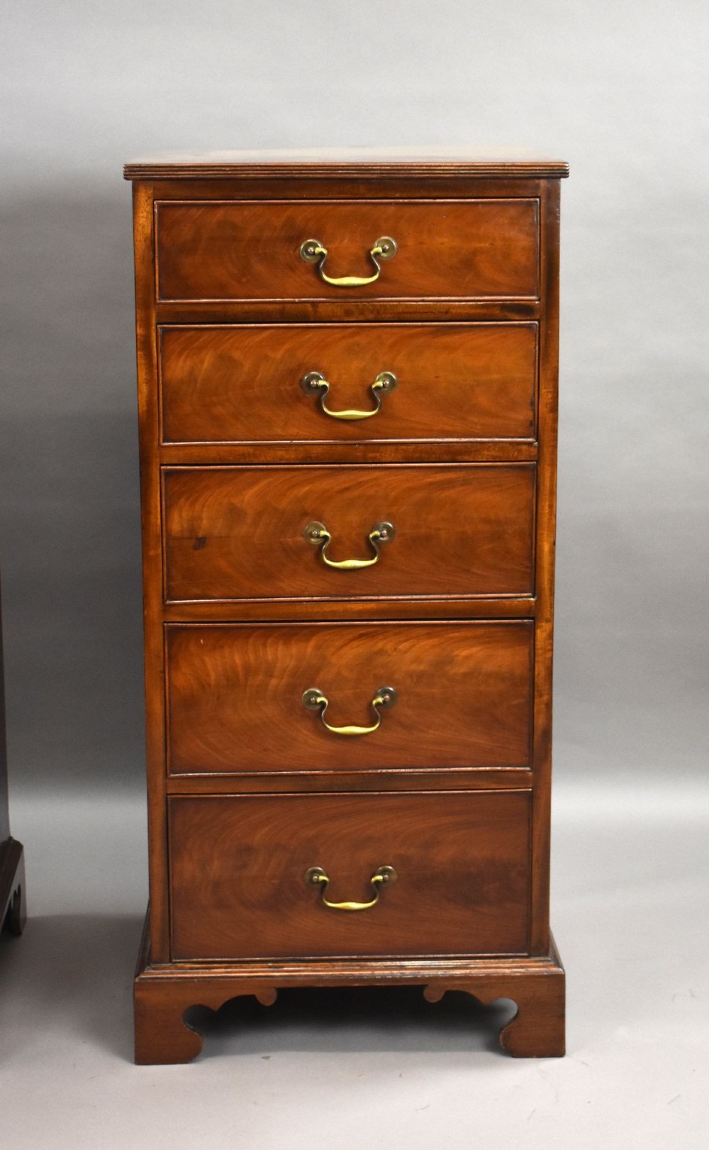 A matching pair of tall, narrow mahogany bedside chests, each featuring five drawers with brass handles and resting on bracket feet. View IV