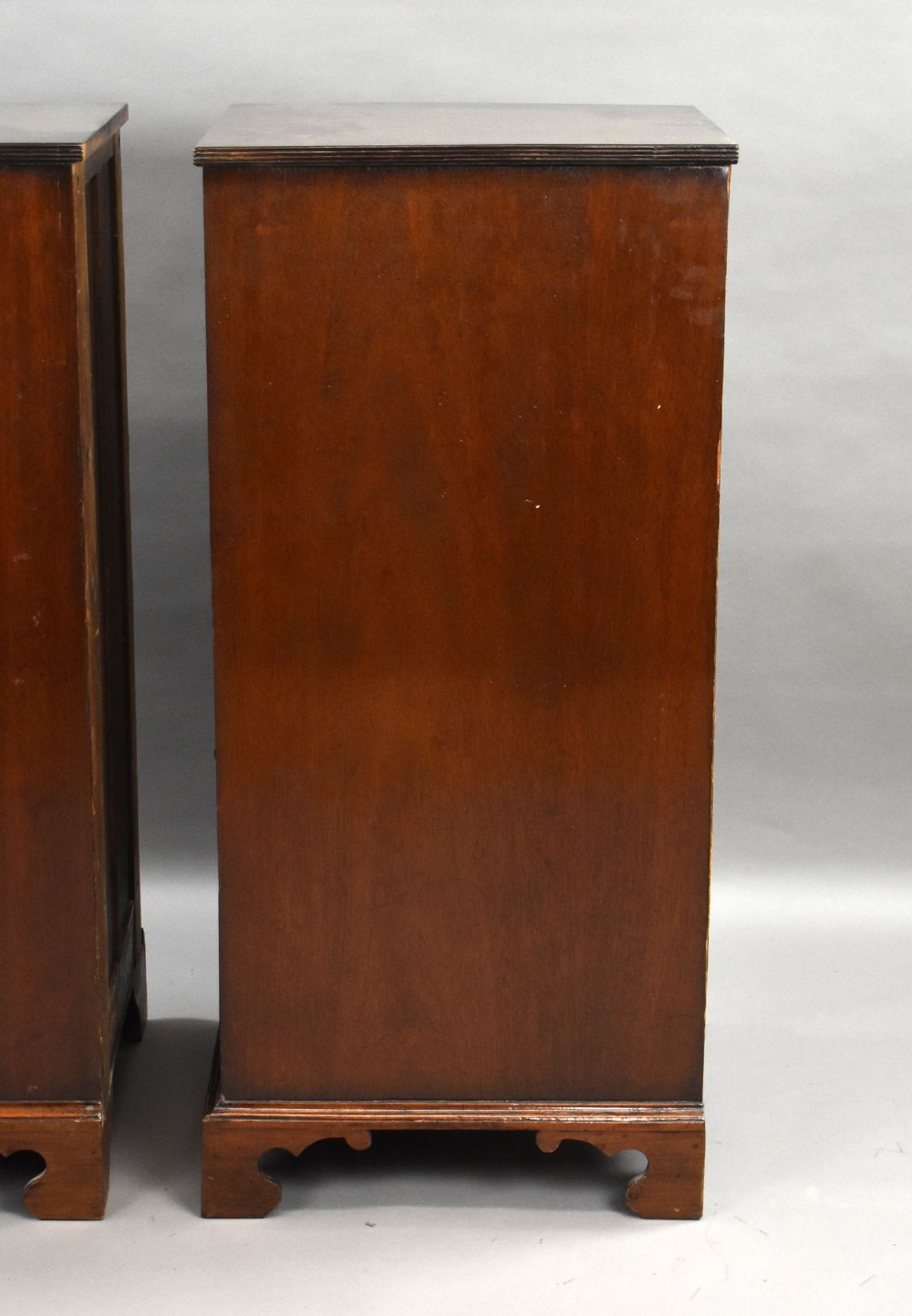 A matching pair of tall, narrow mahogany bedside chests, each featuring five drawers with brass handles and resting on bracket feet. View V