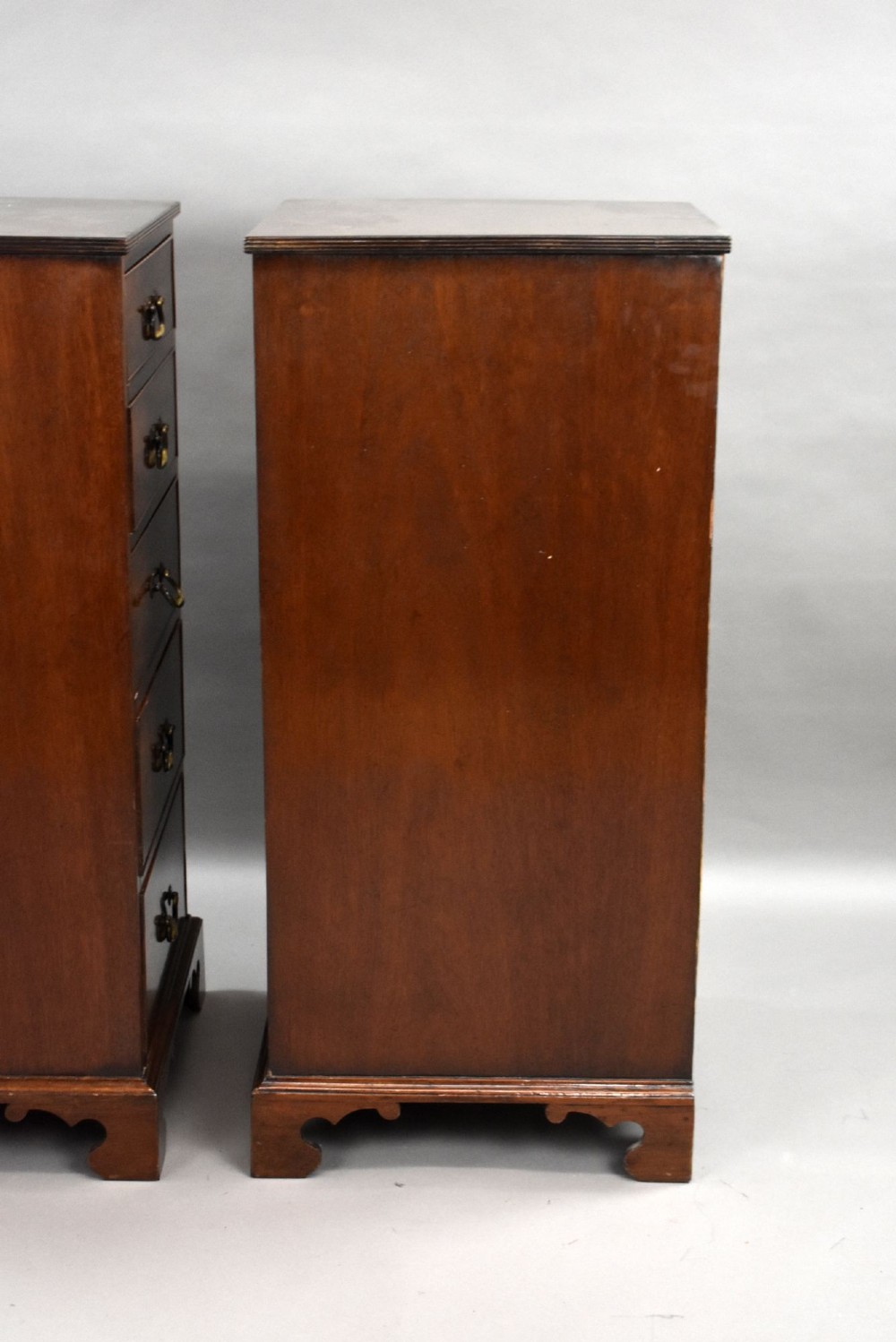 A matching pair of tall, narrow mahogany bedside chests, each featuring five drawers with brass handles and resting on bracket feet. View VI