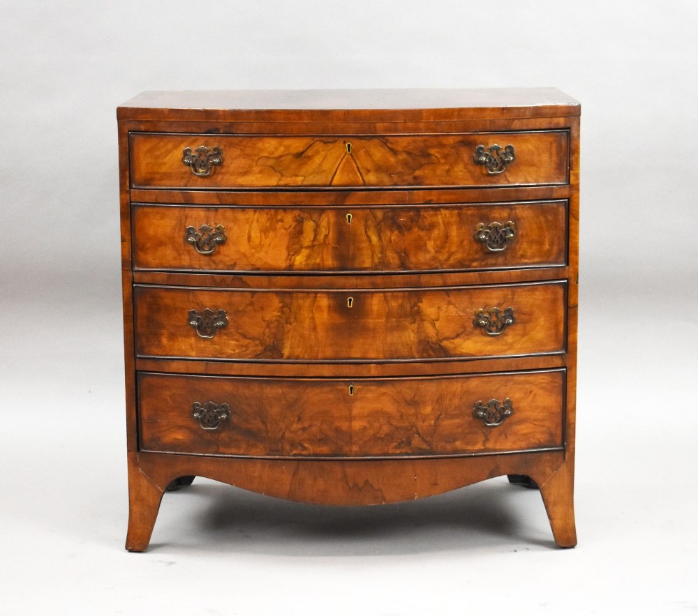 A four-drawer bow front chest made of figured brown walnut with brass handles and shaped bracket feet. View II