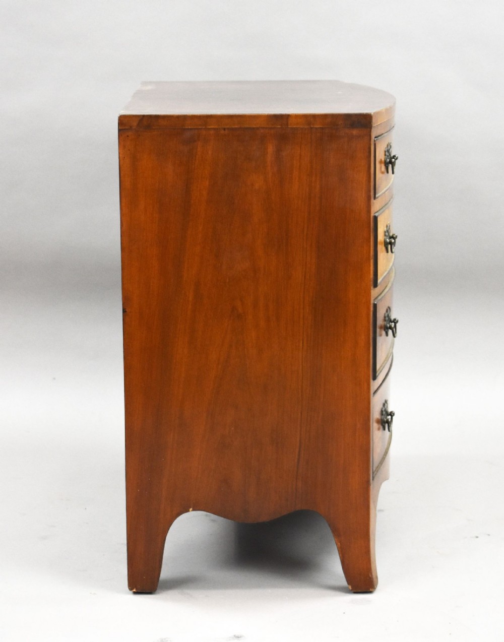 A four-drawer bow front chest made of figured brown walnut with brass handles and shaped bracket feet. View V