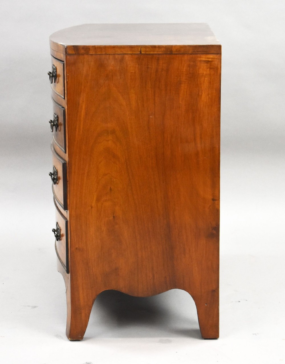 A four-drawer bow front chest made of figured brown walnut with brass handles and shaped bracket feet. View VI