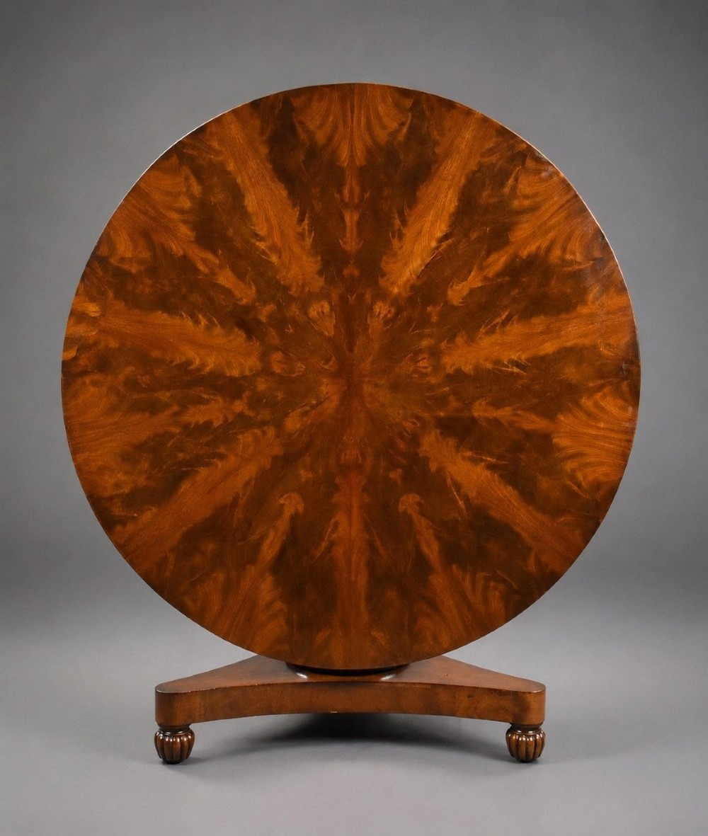 A circular Regency tilt-top breakfast table with starburst flame mahogany veneers shown tilted upright on a pedestal base.
