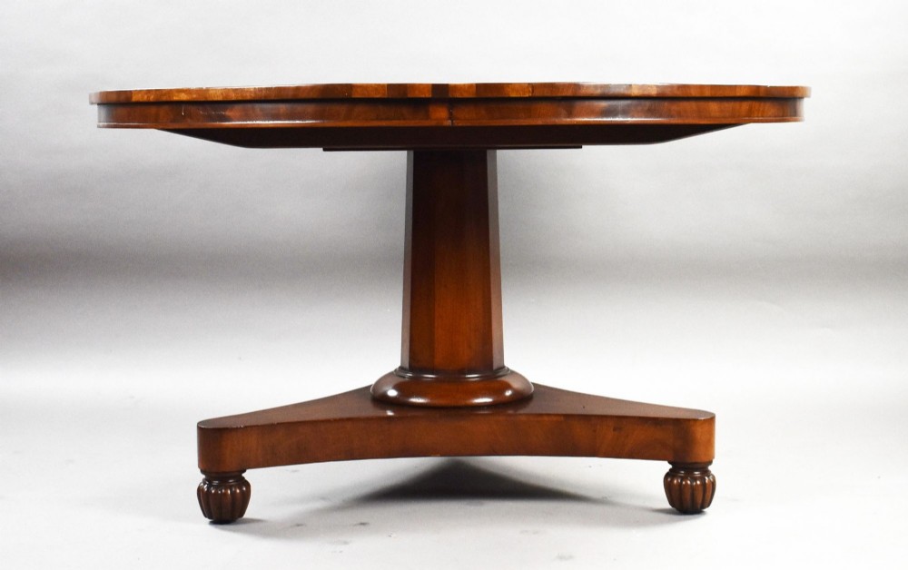 A circular Regency tilt-top breakfast table with starburst flame mahogany veneers shown tilted upright on a pedestal base. View III