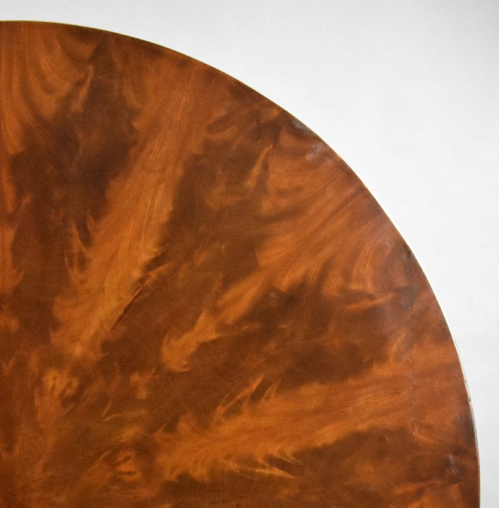 A circular Regency tilt-top breakfast table with starburst flame mahogany veneers shown tilted upright on a pedestal base. View V