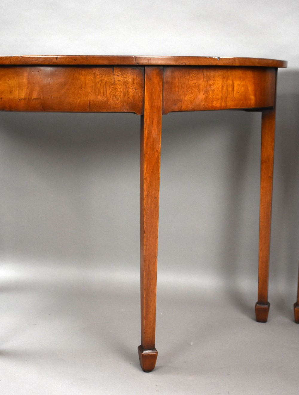 A pair of Georgian mahogany demilune console tables featuring semi-circular tops, plain aprons, and square tapered legs. View VI