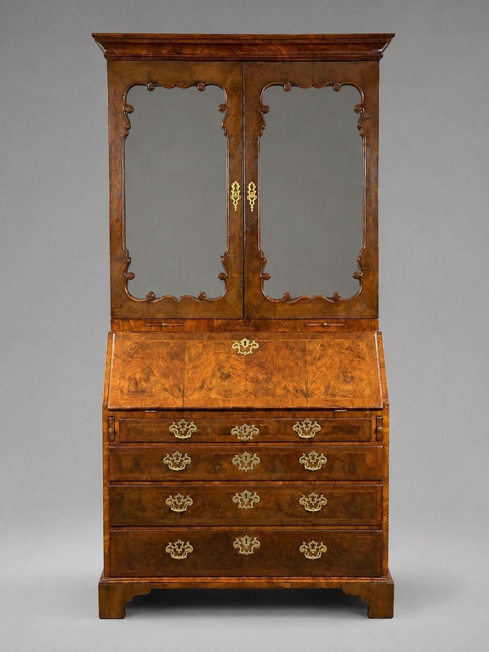 A George II burr walnut bureau bookcase featuring an upper double-door cabinet with shaped mirrored panels over a fall-front desk and four drawers with brass handles.