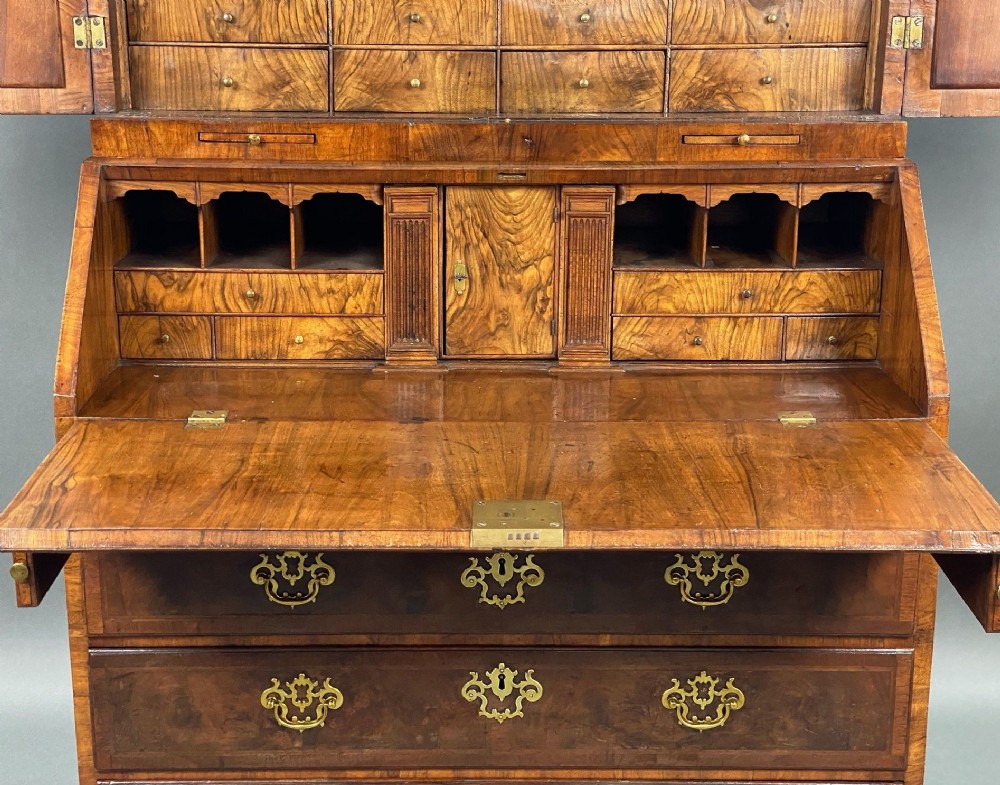 A George II burr walnut bureau bookcase featuring an upper double-door cabinet with shaped mirrored panels over a fall-front desk and four drawers with brass handles. View V