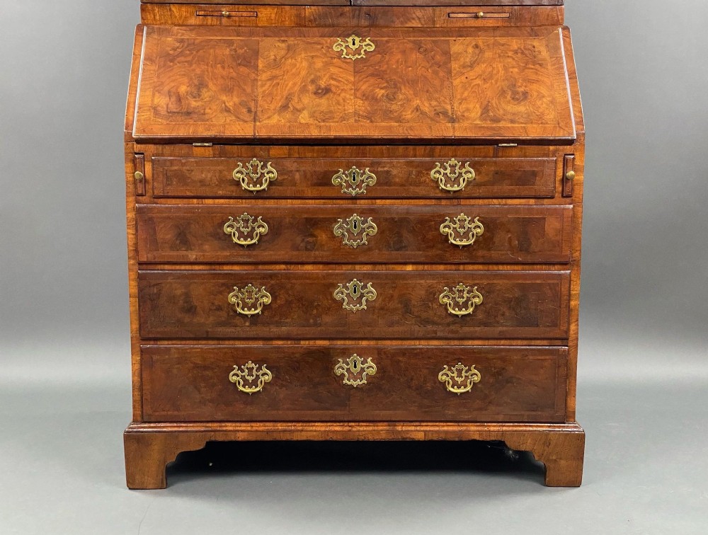 A George II burr walnut bureau bookcase featuring an upper double-door cabinet with shaped mirrored panels over a fall-front desk and four drawers with brass handles. View VII