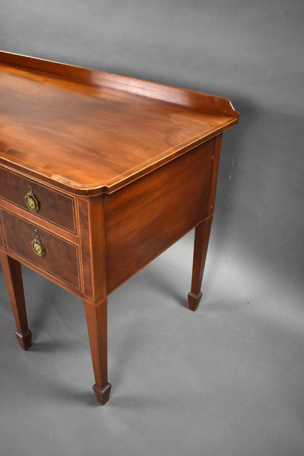 A George III mahogany sideboard featuring an inlaid concave centre, multiple drawers with circular brass handles, and square tapered legs with spade feet. View VI