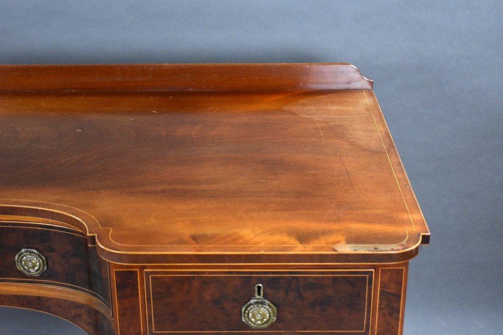 A George III mahogany sideboard featuring an inlaid concave centre, multiple drawers with circular brass handles, and square tapered legs with spade feet. View X