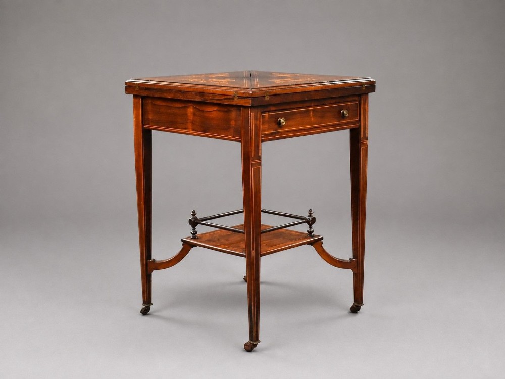 An Edwardian inlaid rosewood envelope card table with tapered square legs, brass castors, a lower undertier shelf, and a top split into four triangular leaves.