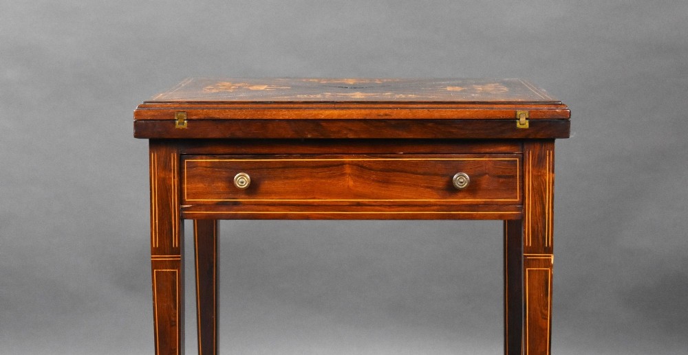 An Edwardian inlaid rosewood envelope card table with tapered square legs, brass castors, a lower undertier shelf, and a top split into four triangular leaves. View IV