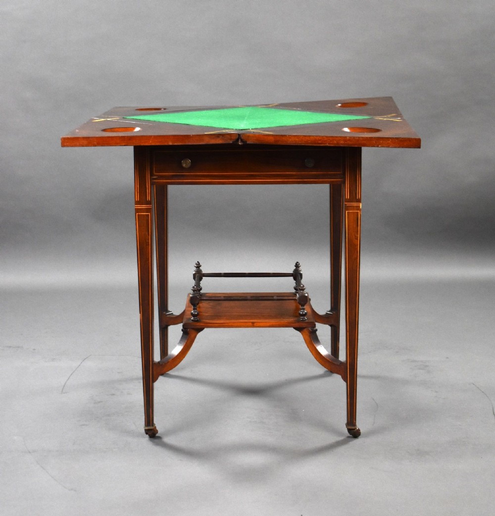 An Edwardian inlaid rosewood envelope card table with tapered square legs, brass castors, a lower undertier shelf, and a top split into four triangular leaves. View VI