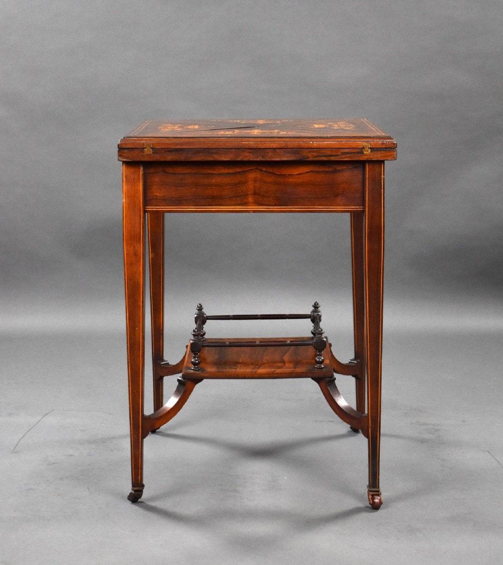 An Edwardian inlaid rosewood envelope card table with tapered square legs, brass castors, a lower undertier shelf, and a top split into four triangular leaves. View IX