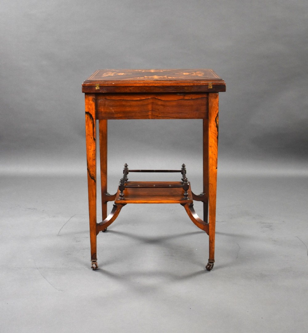 An Edwardian inlaid rosewood envelope card table with tapered square legs, brass castors, a lower undertier shelf, and a top split into four triangular leaves. View X