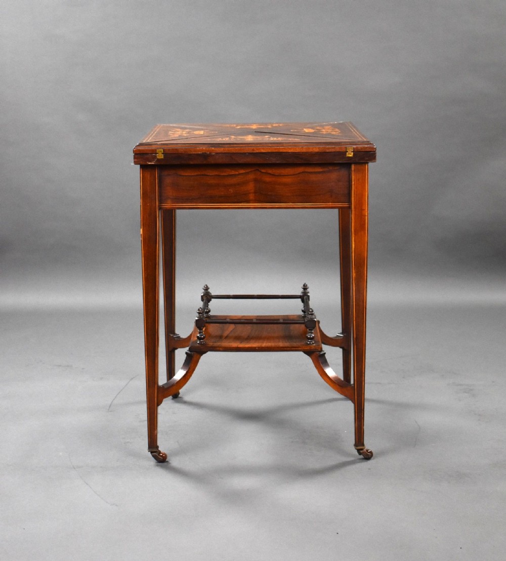 An Edwardian inlaid rosewood envelope card table with tapered square legs, brass castors, a lower undertier shelf, and a top split into four triangular leaves. View XI