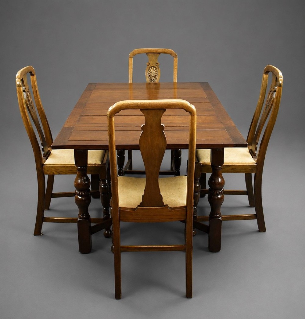 An antique warm brown oak draw-leaf dining table surrounded by four matching carved wooden chairs with light upholstery.