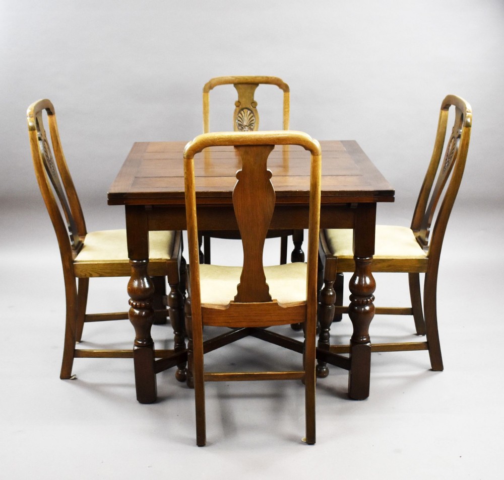 An antique warm brown oak draw-leaf dining table surrounded by four matching carved wooden chairs with light upholstery. View II