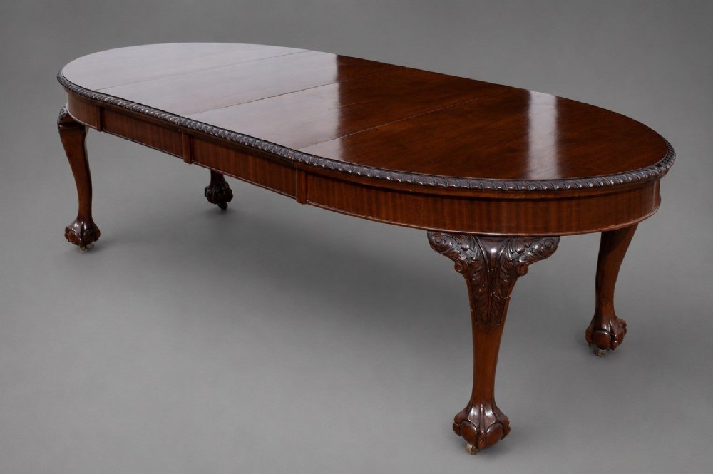 An Edwardian mahogany extending dining table surrounded by matching Chippendale style dining chairs with striped upholstered seats and carved ball and claw feet. View VI