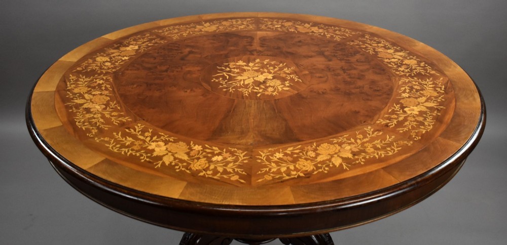 A Victorian circular burr walnut centre table featuring floral marquetry inlays on the tabletop and a dark carved pedestal base. View IV