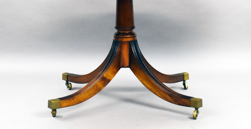 An oval Regency style flame mahogany tilt-top dining table featuring a crossbanded satinwood border and a pedestal base with brass castors. View V
