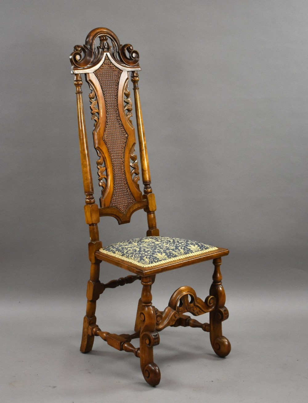 A long dark oak refectory style dining table surrounded by ten high-back carved oak chairs with woven cane back panels and patterned upholstered seats. View III
