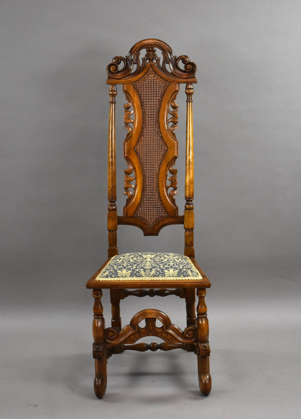A long dark oak refectory style dining table surrounded by ten high-back carved oak chairs with woven cane back panels and patterned upholstered seats. View IV