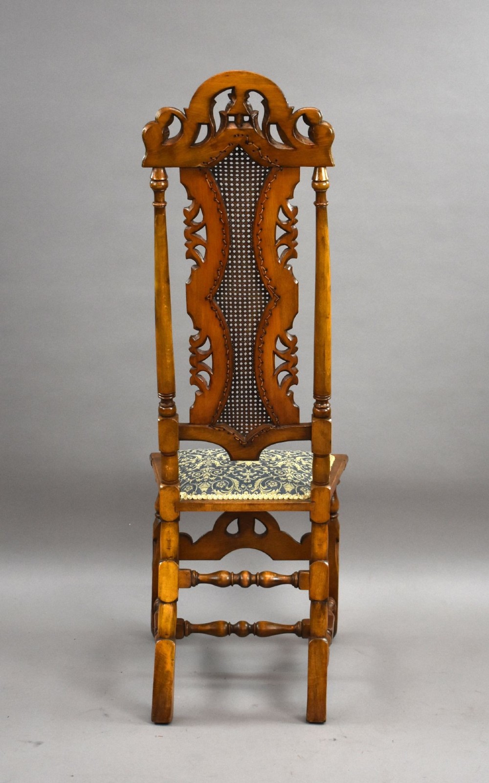 A long dark oak refectory style dining table surrounded by ten high-back carved oak chairs with woven cane back panels and patterned upholstered seats. View VIII
