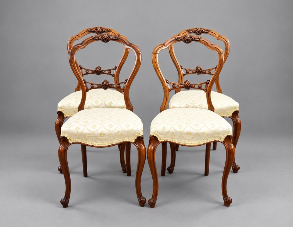 A set of four Victorian walnut balloon back dining chairs with carved horizontal splats, cabriole front legs, and cream pattern upholstered seats.