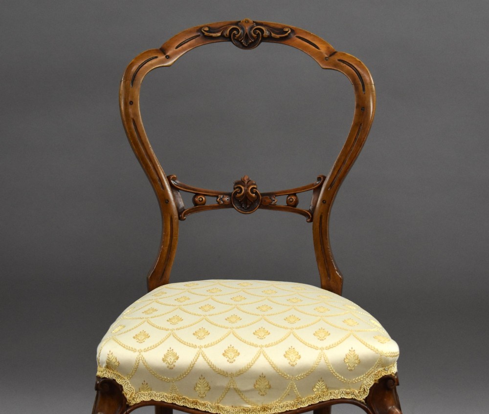 A set of four Victorian walnut balloon back dining chairs with carved horizontal splats, cabriole front legs, and cream pattern upholstered seats. View IV
