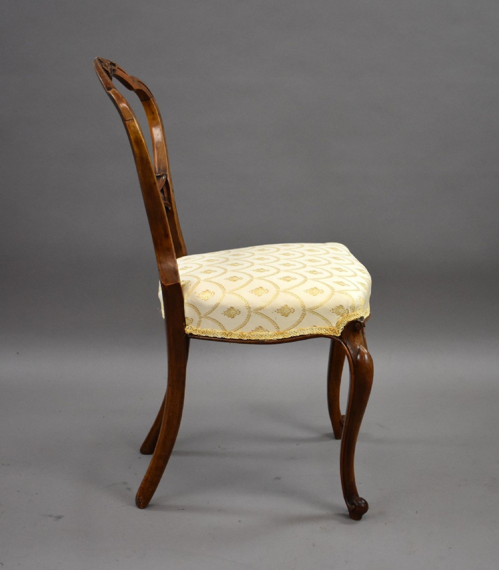 A set of four Victorian walnut balloon back dining chairs with carved horizontal splats, cabriole front legs, and cream pattern upholstered seats. View VI